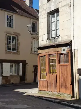 Op de hoek van een straat in Langres waar de zon op een oud winkeltje met een bruine houten pui schijnt met daarboven een antieke straatlantaarn.