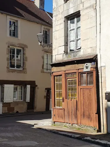 Op de hoek van een straat in Langres waar de zon op een oud winkeltje met een bruine houten pui schijnt met daarboven een antieke straatlantaarn.