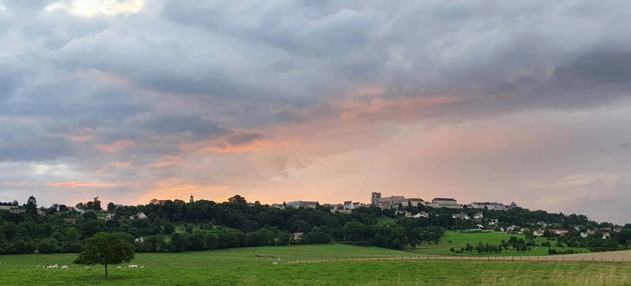 Langres op de berg met een zonsondergang die weerkaatst op de wolken en daardoor een mooie perzik roze gloed geeft aan de wolken met daaromheen donkere grijsblauwe lucht.