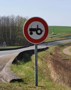 Een leuk verkeersbord waarop een tractor met een mannetje staat (die niet de snelweg op mag) iemand heeft het mannetje een hoge hoed gegeven een er staan rookpluimpjes boven de tractor.